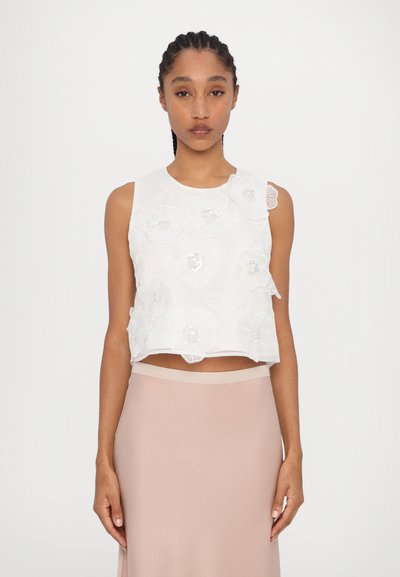 White sleeveless crop top featuring embroidered floral designs with intricate stitching and gem accents, paired with a fitted blush-colored skirt.