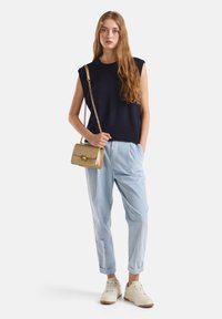 Granatowa bezrękawnikowa bluzka dzianinowa z prążkowanym wykończeniem, jasnoniebieskie plisowane spodnie i mała złota torebka na ramię, zestawione z białymi trampkami.