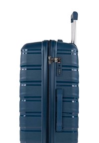 Maleta rígida en azul profundo con ranuras horizontales, doble cremallera, cierre TSA y asa retráctil. Textura suave, diseño duradero.