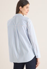 Chemise à rayures bleu clair avec fines lignes orange, manches longues, pli au dos et col classique, confectionnée dans un tissu lisse.