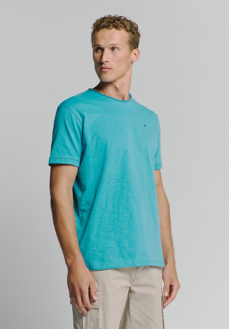 Turquoise t-shirt met korte mouwen en een ronde hals, lichtgewicht textuur en klein logo detail op de borst. Casual fit, gecombineerd met beige shorts.