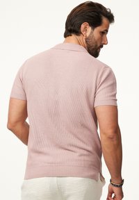 Kurzärmliges Poloshirt aus leichtem pinkem Strickstoff, mit flachem Kragen, gerippten Bündchen und seitlichen Schlitzen am Saum für zusätzlichen Bewegungsraum.