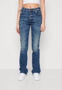 Blue denim jeans with a high waist, five-pocket design, subtle fading, and straight leg fit; paired with white sneakers.