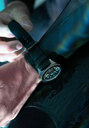 Schwarzes Gummiband an einem Handgelenk, mit einem runden Zifferblatt, schwarzem Ziffernblatt, leuchtenden Markierungen und einer strukturierten Lünette.