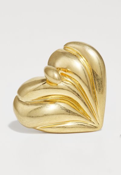 Accessorio a forma di cuore in oro con superficie curva e testurizzata caratterizzata da linee sottili. Presenta un piccolo accento ovale sulla parte superiore. Finitura metallica liscia.