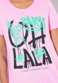 Roze T-shirt met korte mouwen met zwart en mintgroen grafisch tekst: "OH LA LA PARIS" met een afbeelding van de Eiffeltoren en diamantvormen.