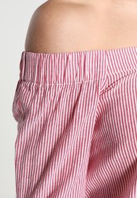 Addome scoperto sopra pantaloni larghi a righe verticali rosso e bianco con vita elastica.