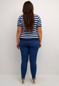 Striped navy og lys blå striktrøje med korte ærmer, parret med mørkeblå tætsiddende jeans og beige sneakers. Stoffet ser glat ud.