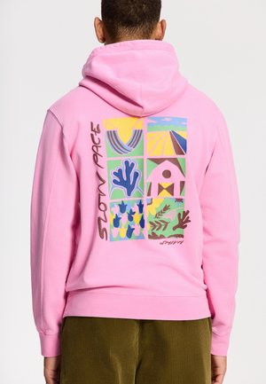Roze hoodie van zacht materiaal met een multiculturele grafisch ontwerp op de achterkant, met abstracte vormen en patronen.