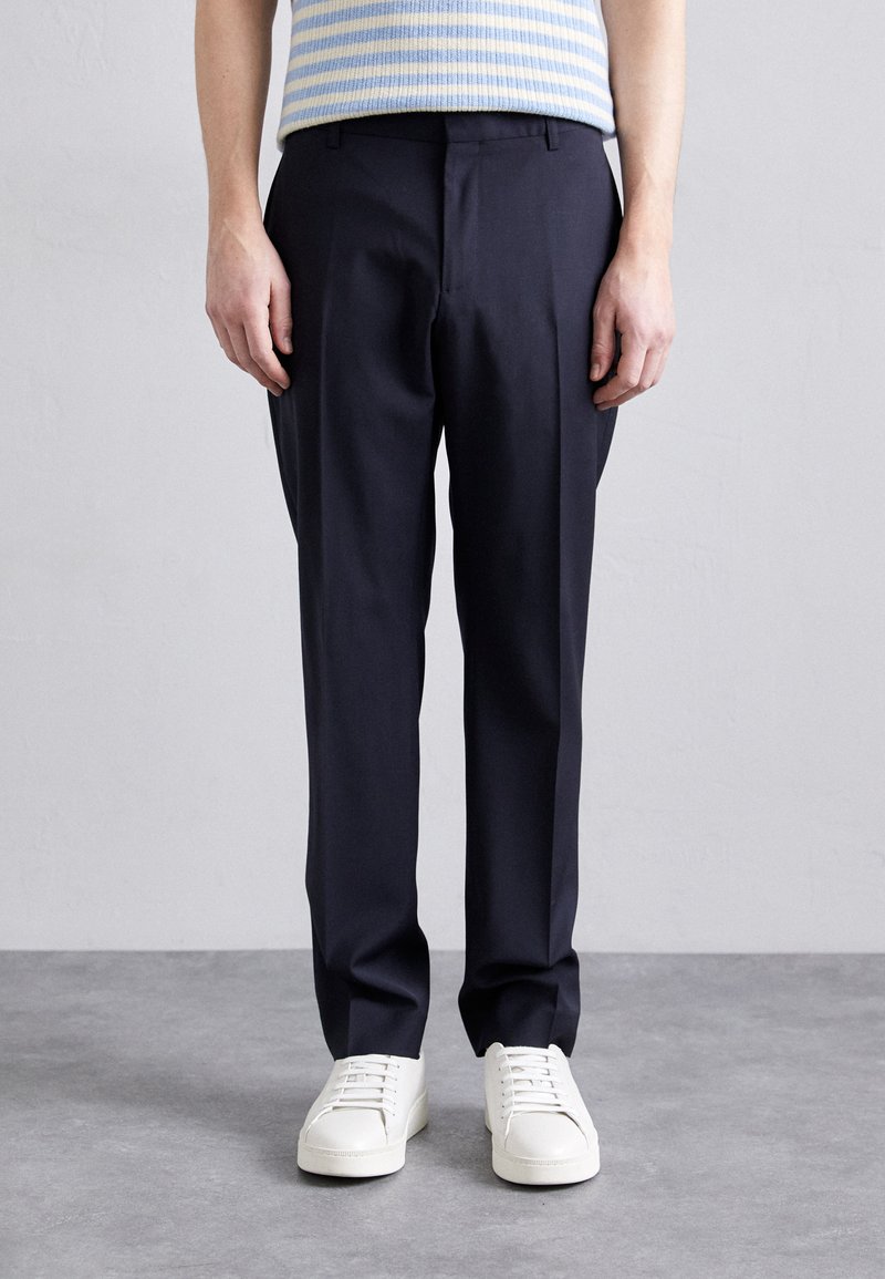 Marine dressbukser med en skreddersydd passform, som har glatt stoff, rene linjer og frontfolder, kombinert med hvite sneakers med lavt skaft.