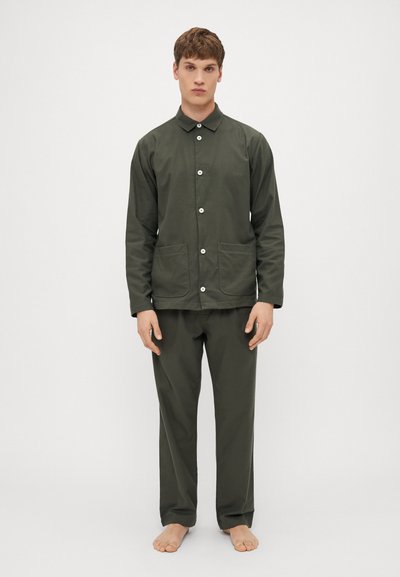 Giacca leggera di un verde scuro, con colletto e bottoni frontali; abbinata a pantaloni larghi coordinati. Tessuto texturizzato, due tasche frontali.
