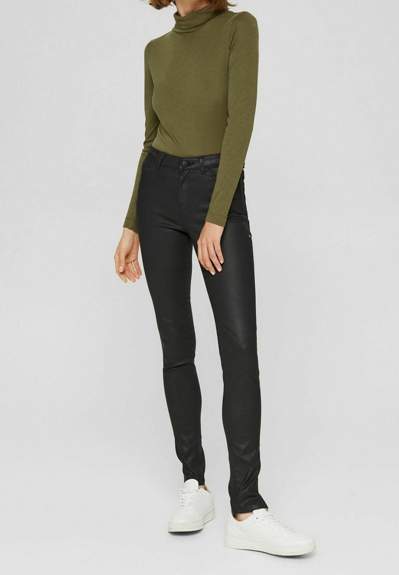 Haut col roulé vert olive associé à un pantalon noir ajusté et des baskets blanches. La tenue présente une texture lisse et un design élégant.