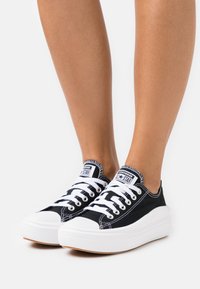 Zwarte canvas sneakers met witte rubberen zolen en veters, voorzien van een ronde neus en contrasterende stiksels. Merketiket op de tong.