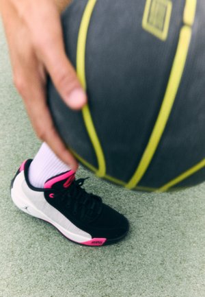 Mustad ja hallid korvpallijalatsid roosa aktsentide ja paeltega. Näha on valge sokk. Käsi hoiab musta korvpalli, millel on kollased triibud.