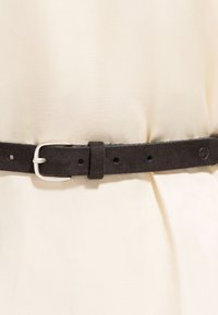 Ceinture en suède noir avec boucle en argent fix�ée sur un fond en tissu beige.