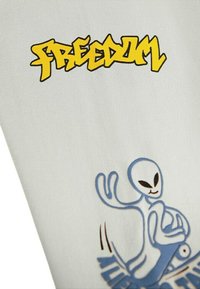 Bílý materiál s žlutým graffiti stylem písma "SVOBODA" a modrou ilustrací mimozemšťana na skateboardu.