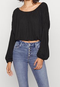 Svart kort topp med elastiskt halsringning och långa puffärmar, matchad med högmidjade blå denimjeans med knappstängning framtill.