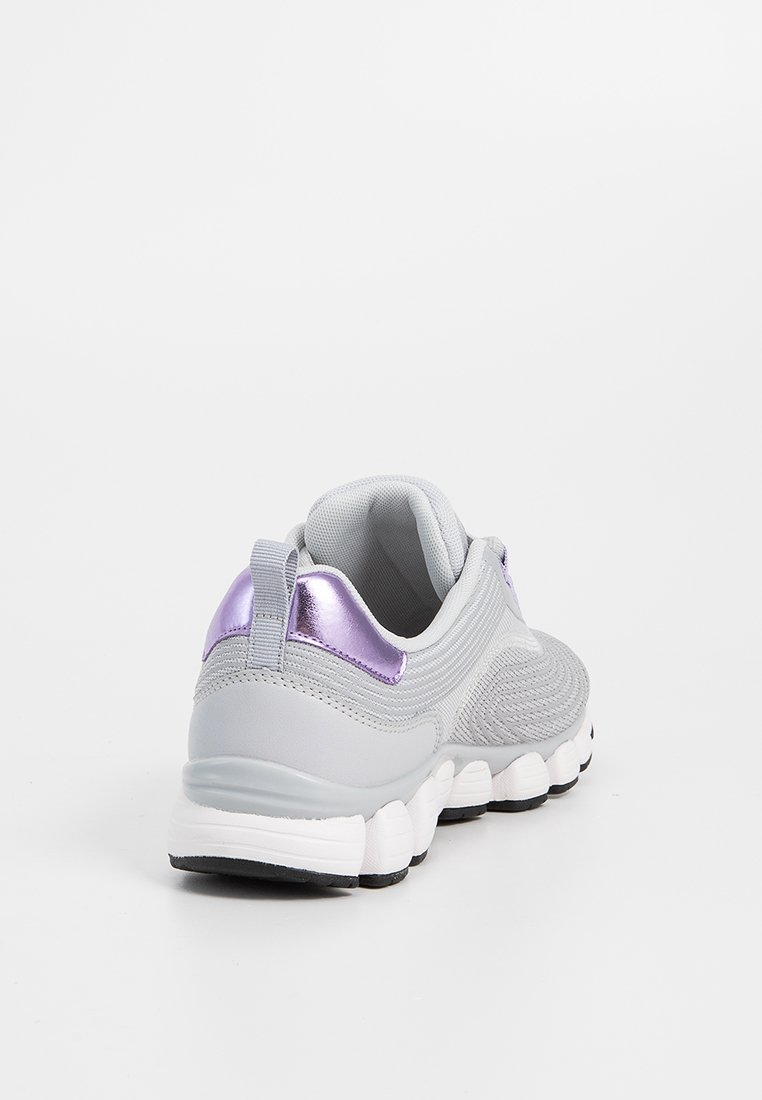 Scarpa atletica grigio chiaro con suola bianca segmentata e accentuazione metallica viola sul tallone, mostrata da un'angolazione posteriore a tre quarti su sfondo bianco.