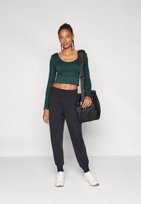 Grønn, cropped langermet topp, sorte joggebukser, hvite sneakers med gummisåler, og en svart skulderveske med et frontlomme i mesh.
