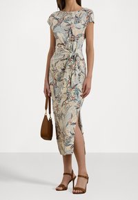 Šaty s květinovým vzorem, ke kolenům, z lehké látky, s páskem na zavázání, krátkými rukávy a bočními rozparky. Hnědé sandály na podpatku a kabelka.