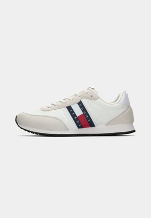 Baskets blanches et beiges avec une finition en daim et en cuir, présentant des rayures bleu marine, rouge et blanches ainsi qu'une semelle en caoutchouc noir. Marque Tommy Jeans visible.