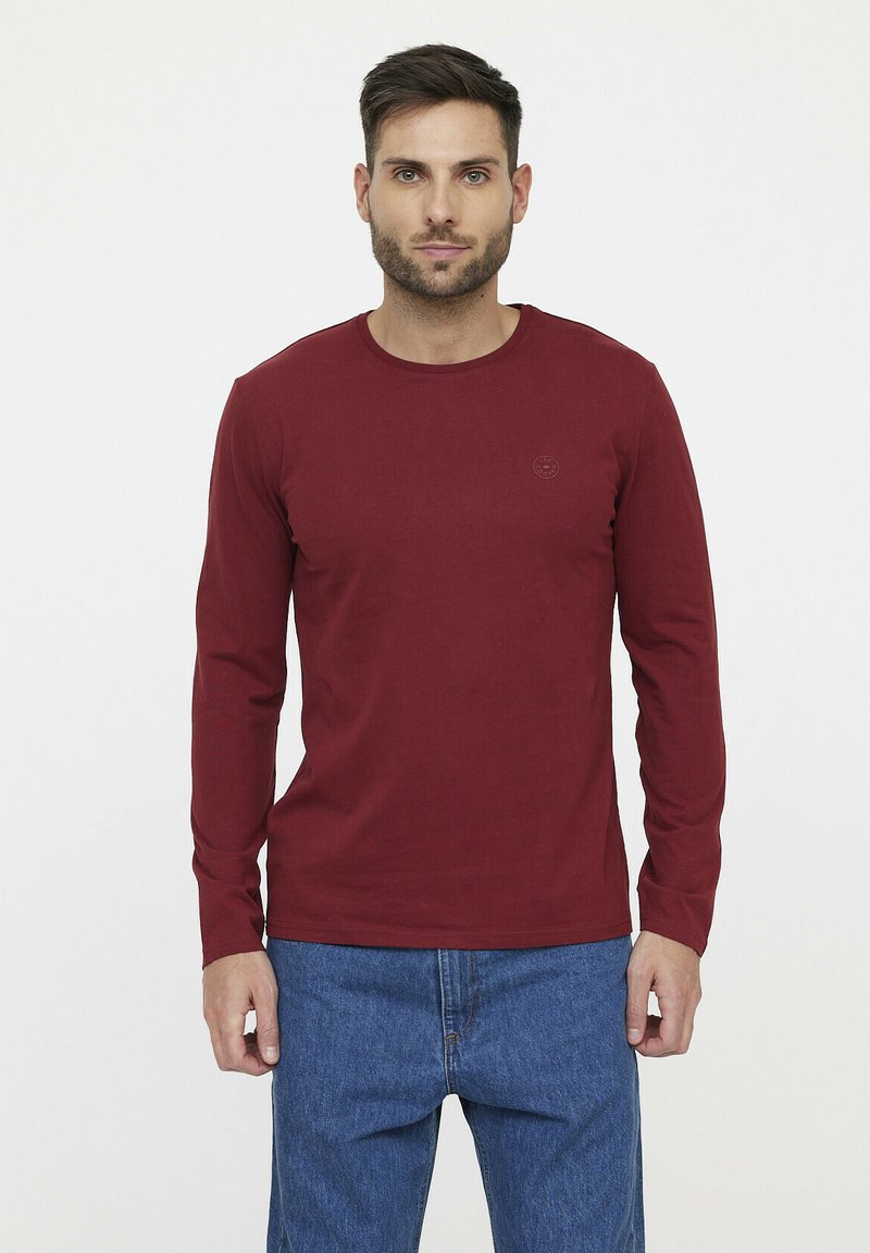 Lange mouwen, bordeauxrood katoenen t-shirt met een ronde halslijn en een klein logo op de borst, gecombineerd met een blauwe spijkerbroek. Gladde textuur.
