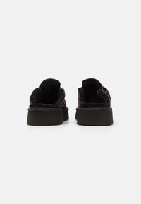 Scarpe slip-on nere con un interno morbido e peloso e una suola spessa e testurizzata. La parte superiore presenta un design stampato e bordi arrotondati.