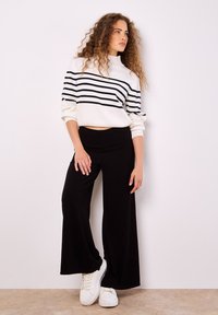 Witte en zwarte gestreepte trui met een hoge hals en cropped pasvorm, gecombineerd met zwarte wijde broek en witte sneakers. Soepele textuur.