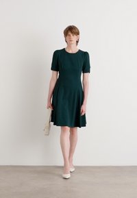 Dark green, short-sleeved dress with a fitted bodice and flared skirt. Smooth fabric, round neckline, and soft pleats at the waist.