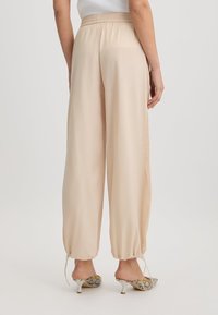 Pantaloni beige a gamba larga realizzati in tessuto leggero, con polsini con cordoncino e pannelli laterali in rete, abbinati a scarpe con tacco alto a fantasia.