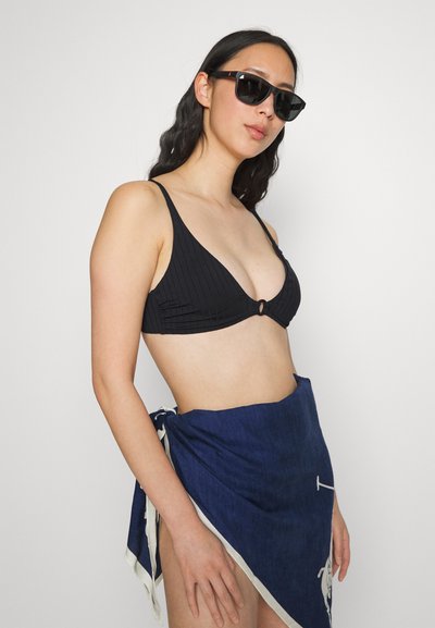 Top de biquíni preto canelado com formato triangular e detalhe em anel central, combinado com uma saia envolvente azul-marinho com acentos brancos e laços.