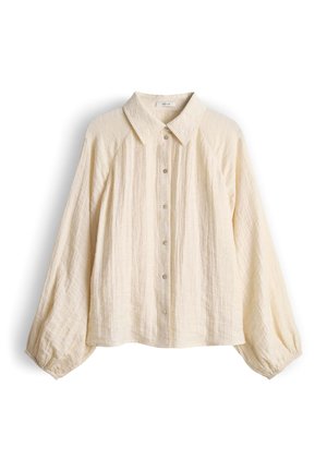 Blouse à manches longues couleur crème avec col pointu, fermeture boutonnée sur le devant et tissu légèrement texturé, présentée à plat sur un fond blanc.
