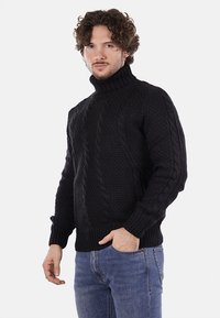 Maglione nero a collo alto, lavorato a maglia con pattern testurizzati e polsini a coste. Abbinato a jeans blu, silhouette aderente e lunghezza media.