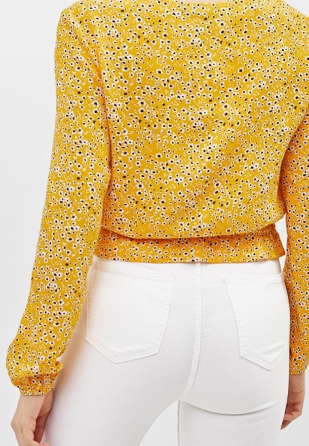 Gul blommig blus med långa ärmar och en insydd midja. I kombination med figursydda vita byxor som har en mjuk, lätt textur.