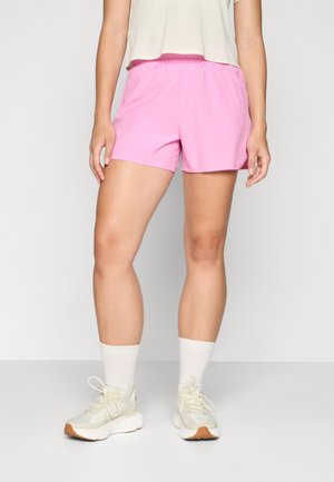 Pantalones cortos deportivos rosas con cinturilla elástica, que presentan una textura suave y un corte relajado, combinados con calcetines blancos hasta la altura del tobillo y zapatos claros.