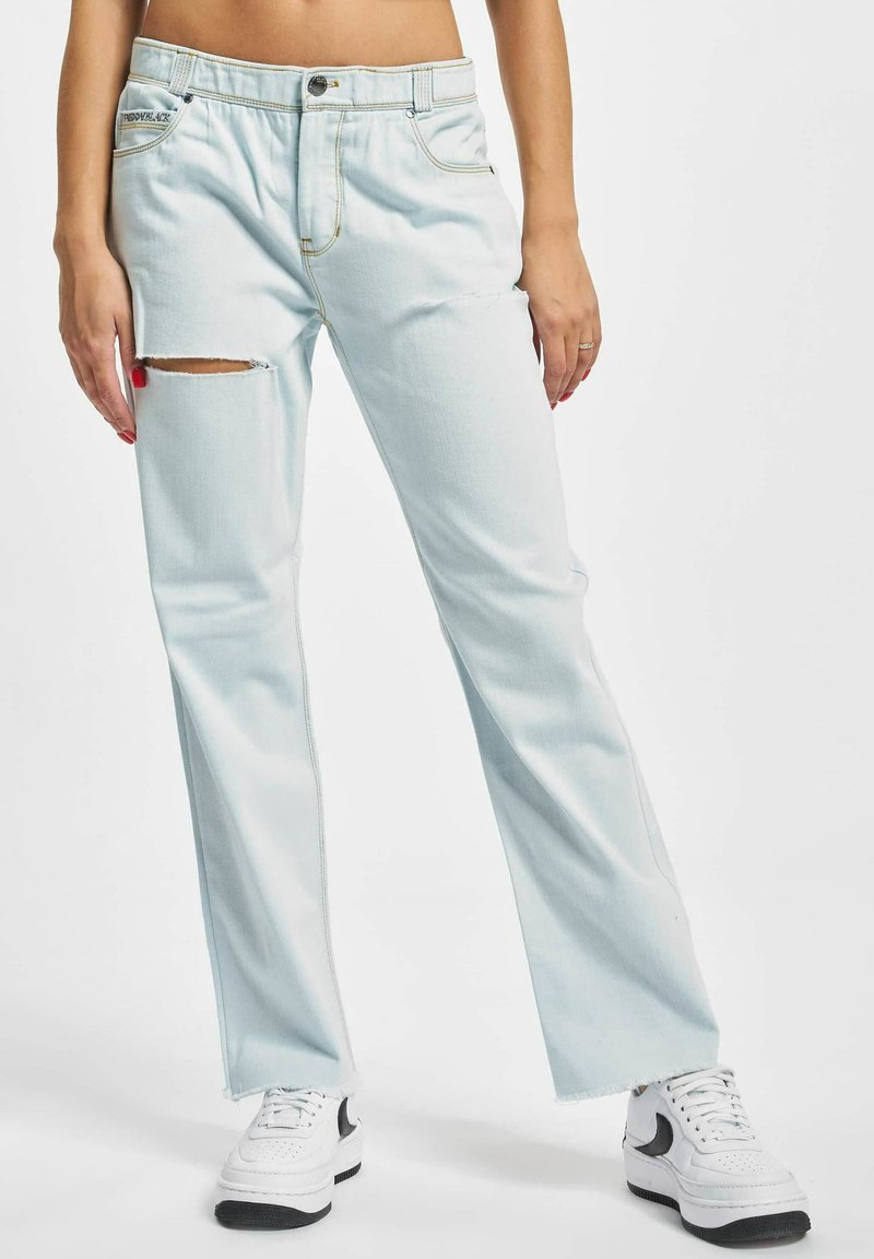 Lyseblå denimjeans med en avslappet passform, som har et lite utsnitt på venstre låret og kontrastsømmer, sammen med hvite sneakers.