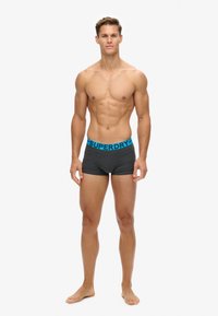 Boxer cortos grises con un logotipo azul de "SUPERDRY" en la cinturilla. Fabricados con tejido suave, diseñados para ofrecer comodidad y un ajuste ceñido.