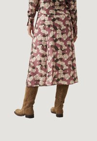 Falda midi floral en rosa con flores blancas y verdes, hecha de un tejido suave. Combinada con botas de ante marrón hasta la rodilla.