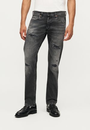 Herrens blekta svarta tajta jeans med slitna revor, använda med svarta läderloafers och en vit skjorta.