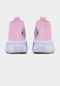 Ροζ ψηλά αθλητικά παπούτσια Converse All Star, ορατά από πίσω, με λευκές σόλες και λογότυπα της μάρκας στη φτέρνα και στις πλευρές.