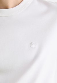 Hvid bomulds T-shirt med en blød tekstur og et lille broderet logo på venstre bryst. Rund halsudskæring med forstærket syning.