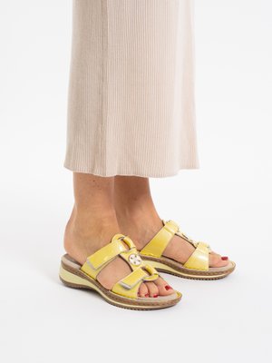 Feet wearing yellow open-toe sandals with adjustable straps and a low wedge heel, paired with a beige ribbed skirt.