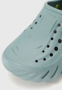 Hellblaue Crocs-Schuhe aus strukturiertem Schaumstoffmaterial, mit Belüftungsöffnungen und einem abgerundeten Zehendesign. Akzente umfassen subtile Linien.