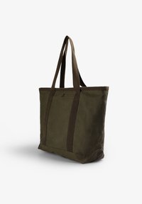 Bolsa de lona verde oliva con asas de tela marrón duales, forma rectangular y un logo sutil en la parte frontal. Diseño duradero y amplio.