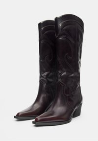 Bottes de cowboy en cuir bordeaux, à hauteur de genou, avec bout pointu, couture décorative et talon empilé. Texture lisse et design détaillé.