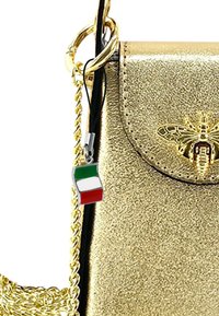 Handtasche aus goldfarbenem Leder mit einer Kettenriemen, die ein Bienenemblem und einen Charm der italienischen Flagge in Grün, Weiß und Rot zeigt.