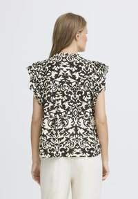 Blusa a righe bianco e nero con maniche a volant, caratterizzata da un design ornato e una vestibilità leggermente rilassata. La vista posteriore mostra la lunghezza del capo.