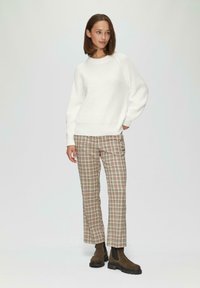 Witte gebreide trui met geribbelde textuur, gecombineerd met een geg checkte broek in beige, bruin en rood. Bruine enkellaarsjes met een gestructureerde zool.