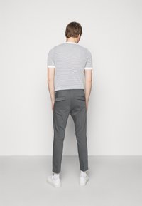 Grijze broek met twee achterzakken, gecombineerd met een lichtgrijs gestreept kortärmelig overhemd en witte sneakers. Eenvoudig en strak ontwerp.