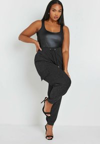 Svart bodysuit med rundad halsringning, i kombination med texturerade svarta jogger-byxor med dragsko i midjan och ankle cuffs. Svarta högklackade skor.